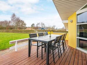 Eine Terrasse mit Tisch und Stühlen, einem weißen Geländer und Blick auf ein grünes Feld sowie Häuser im Hintergrund.