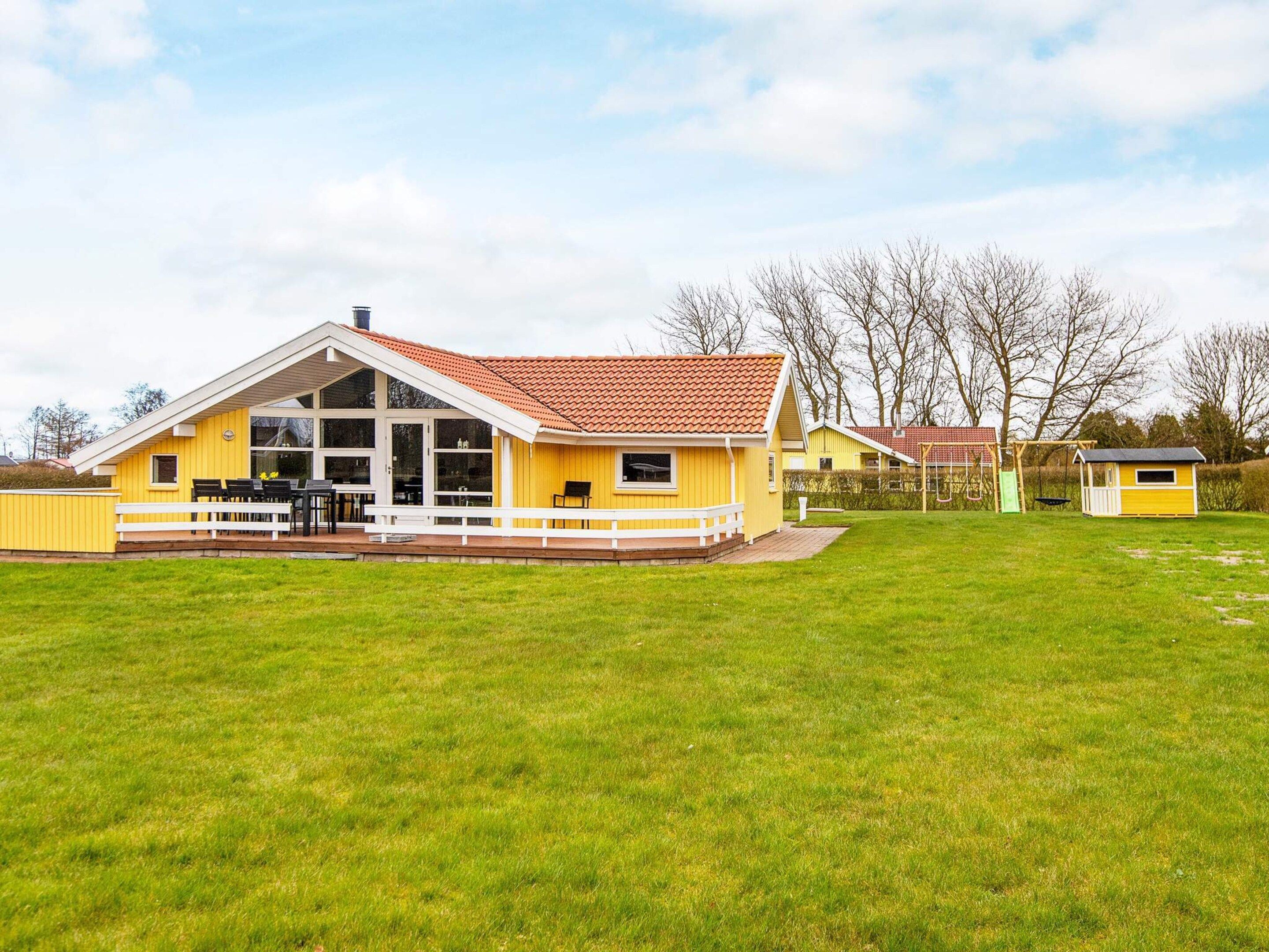 A yellow house with a red roof, a deck, and a grassy yard.