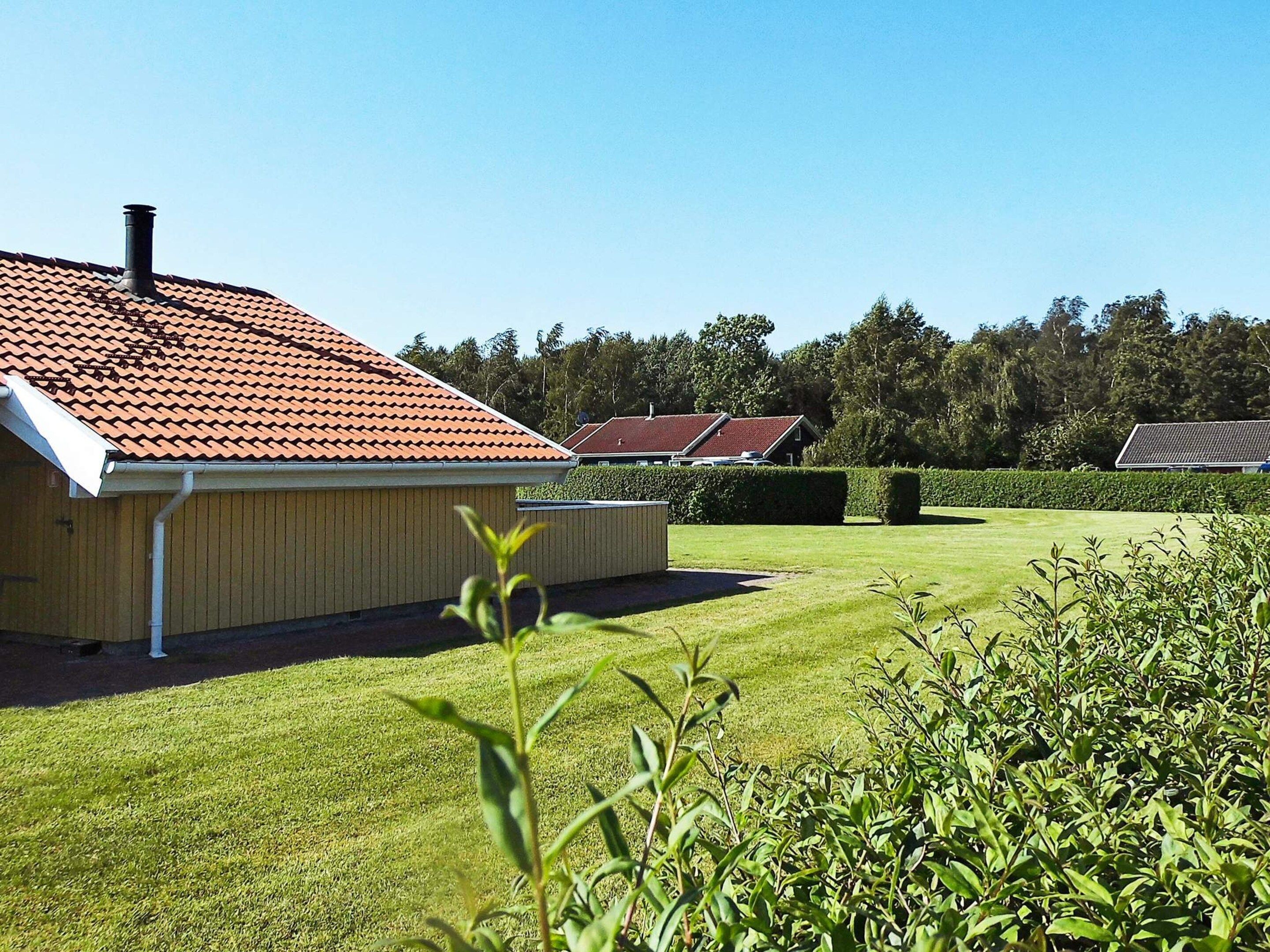 En bostadsbyggnad med ett rött tegeltak, en välskött gräsmatta och en häck i förgrunden.