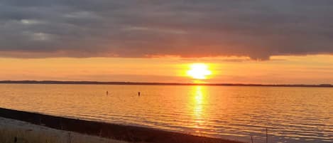 A sunset over a body of water with a distant shoreline and overcast sky.