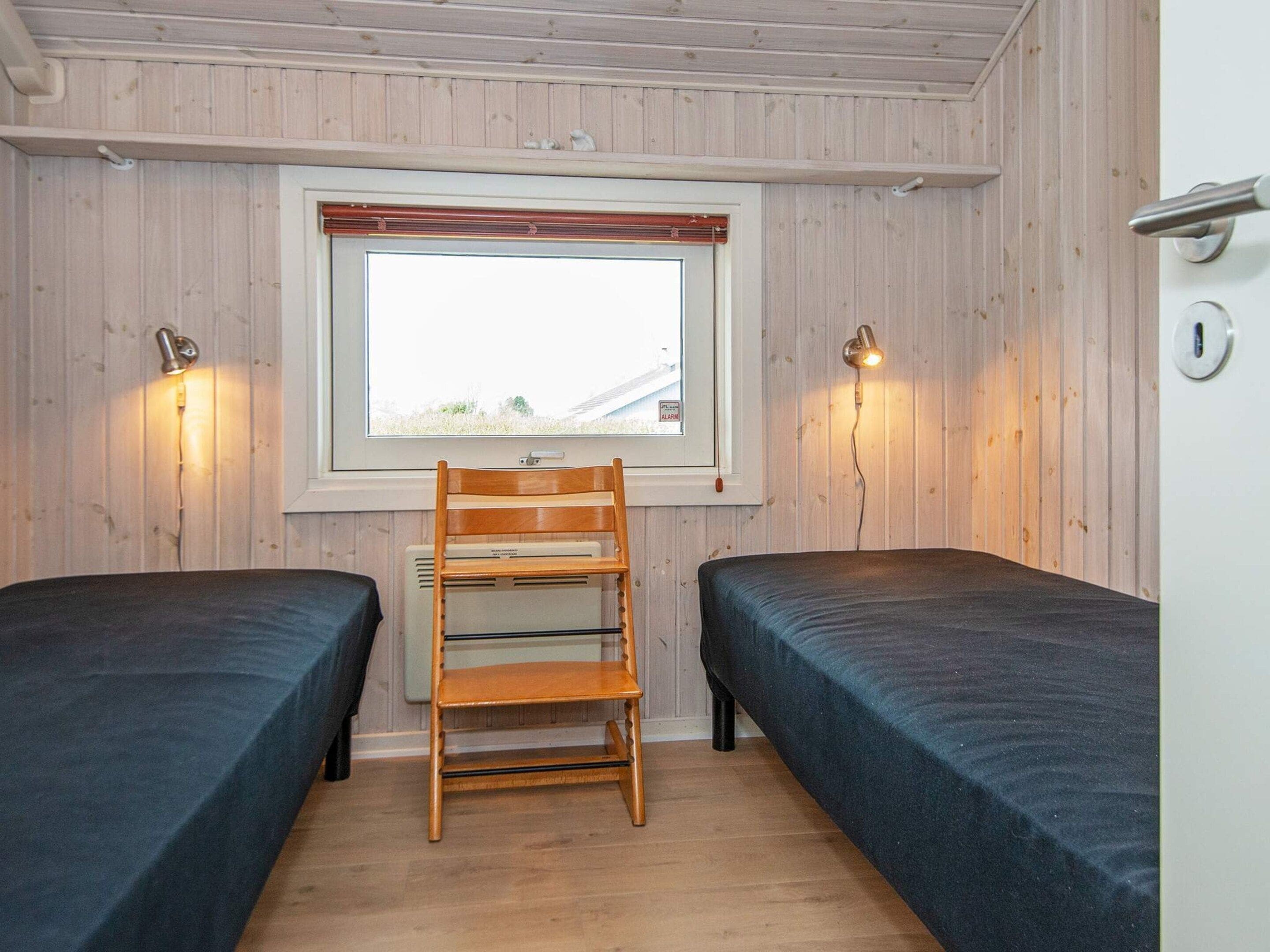 A room with two beds, a wooden chair, a window with a view, and two wall-mounted lamps.