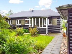 Et sort hus med hvide detaljer, en overdækket veranda og en have med bregner og en sti.