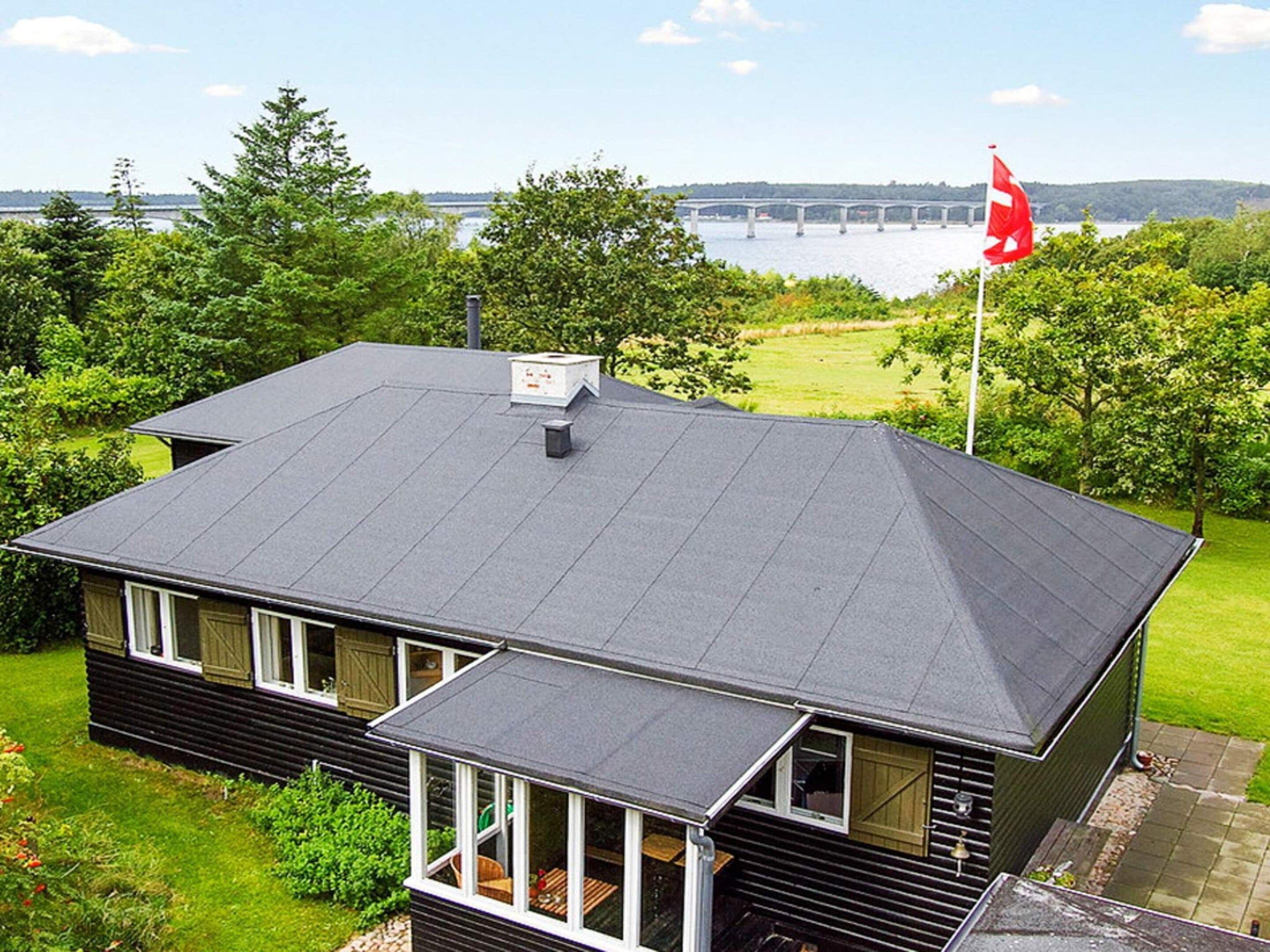 Une maison avec un toit sombre, une cheminée et un mât sur lequel flotte un drapeau.