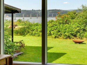 Vista per una finestra d'un jardí amb gespa, un pont a la distància, un cavall i vegetació densa.