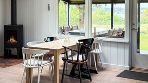 Um quarto aconchegante com uma mesa de madeira, cadeiras, lareira e vista para o verde lá fora.