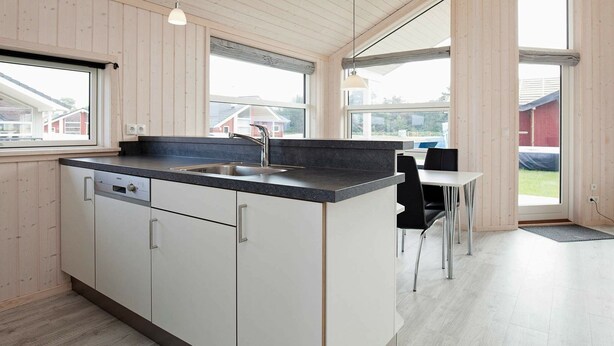 A modern kitchen with a central island, a sink, and a dining area with a table and chairs. - Holiday Home in Großenbrode (Grossenbrode)