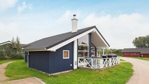 A small, single-story building with a dark blue exterior and a white porch. - Holiday Home in Großenbrode (Grossenbrode)
