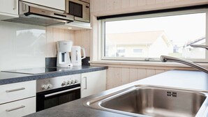 A modern kitchen with white cabinets, a stainless steel sink, a coffee maker, and a window with a view of houses. - Holiday Home in Großenbrode (Grossenbrode)