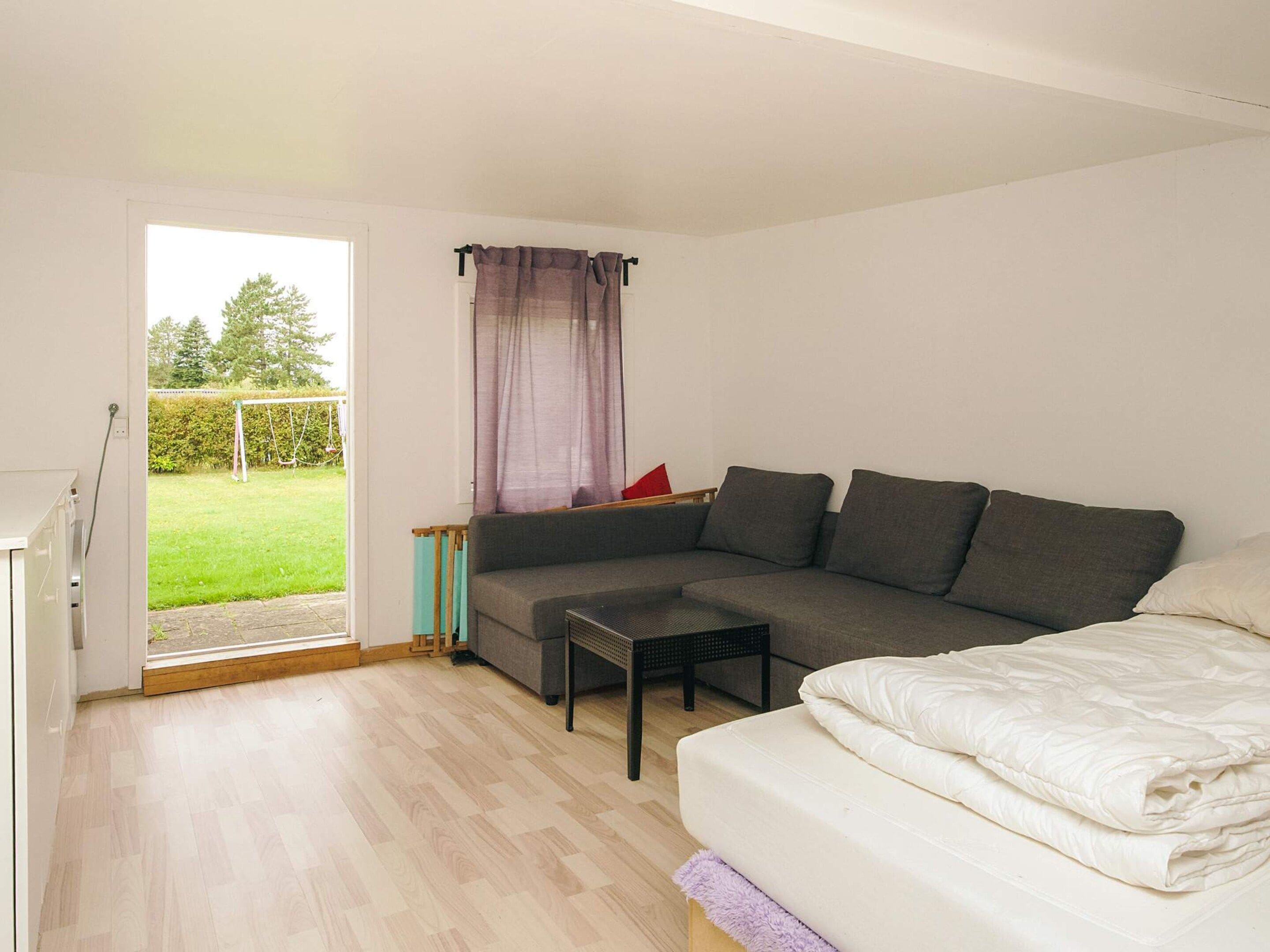 A modern living room with a grey sectional sofa, a small coffee table, and a bed with white bedding.