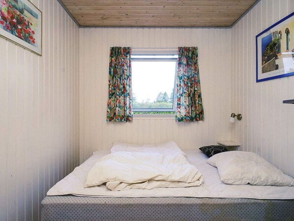 Un dormitorio con cama, una ventana con cortinas, una mesita de noche y una lámpara.
