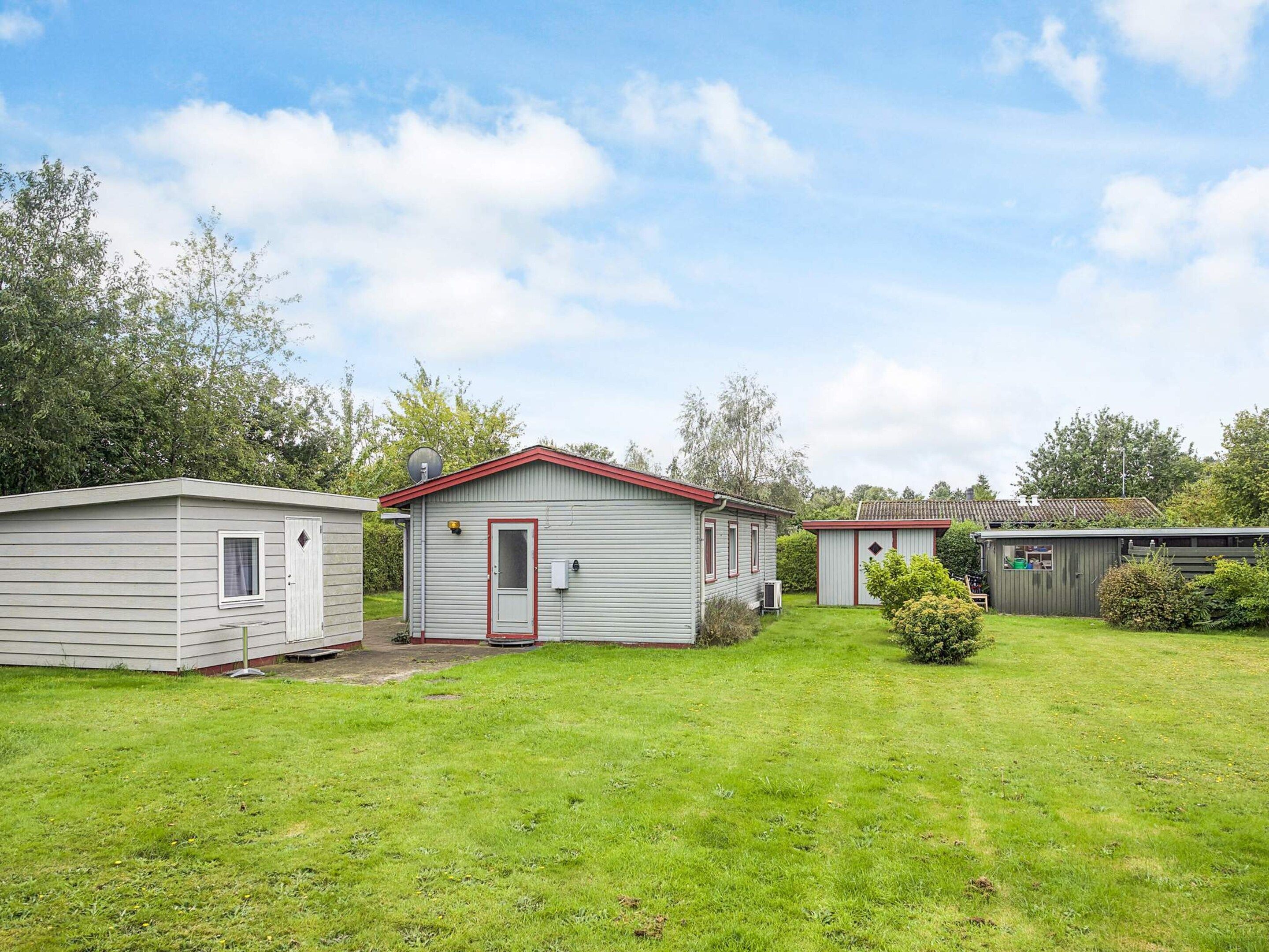 A row of small, single-story mobile homes with red trim and a grassy yard.