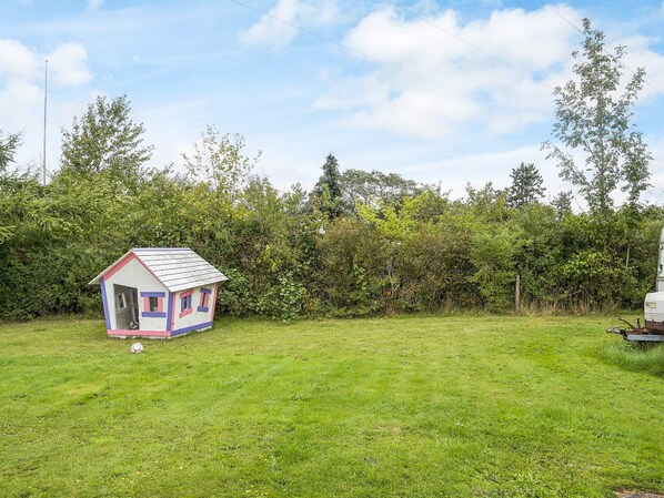 A small, colorful house with a pitched roof and a door, situated in a grassy field with dense bushes and trees in the background. - 6 Person Holiday Home in Eskebjerg-by Traum (Eskebjerg)