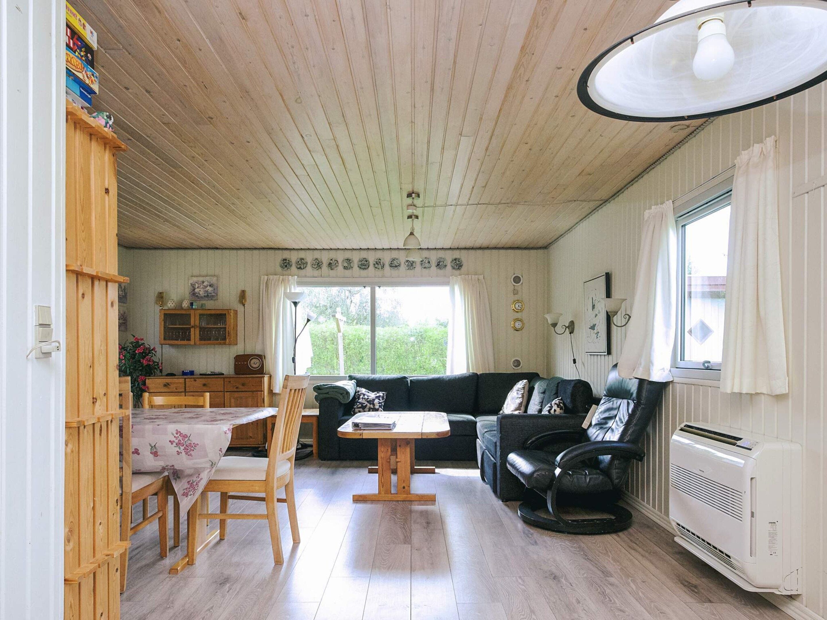 Una sala de estar acogedora con techo de madera, comedor con mesa y sillas, sofá y radiador.