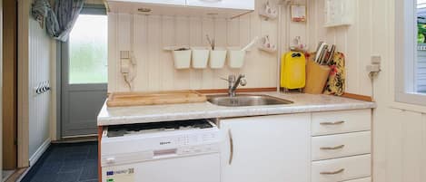 A kitchen with white cabinets, a stainless steel sink, a dishwasher, and a window with a view of greenery outside.