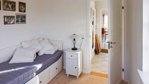 Un dormitorio con cama, mesita de noche, lámpara y una puerta que da a otra habitación.