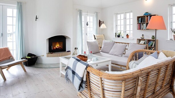 Un salón acogedor con chimenea, muebles de mimbre, una estantería y una lámpara.