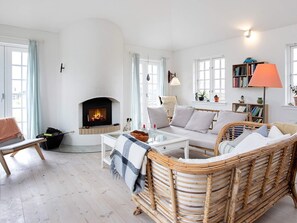 Een gezellige woonkamer met een open haard, rieten meubels, een boekenplank en een lamp.