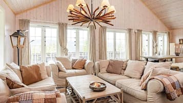 Una sala de estar acogedora con techo alto, vigas de madera y un candelabro central. Hay dos sofás y una mesa de centro con una vela.