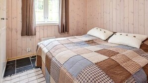 A bedroom with a wooden paneled wall, a window with curtains, a bed with a quilt, and a door with a handle. - 4 Star Holiday Home in Favang (Ringebu)