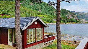 A red cabin with large windows, a deck, and a view of a lake and mountains. - 6 Person Holiday Home in Sundlandet (Hitra)