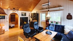 A cozy cabin interior with a wooden ceiling, a fireplace, a dining table, and a blue sofa. - 6 Person Holiday Home in Sundlandet (Hitra)