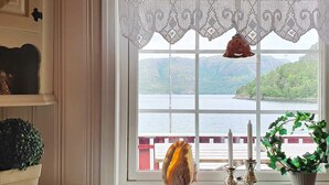 A room with a large window, a decorative lace valance, a candle holder, and a potted plant. - 6 Person Holiday Home in Sundlandet (Hitra)
