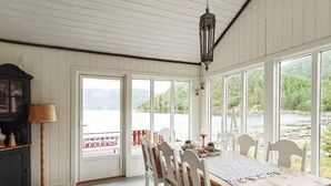 A dining area with a wooden table and white chairs, large windows offering a view of a lake and forest, and a hanging lantern. - 6 Person Holiday Home in Sundlandet (Hitra)