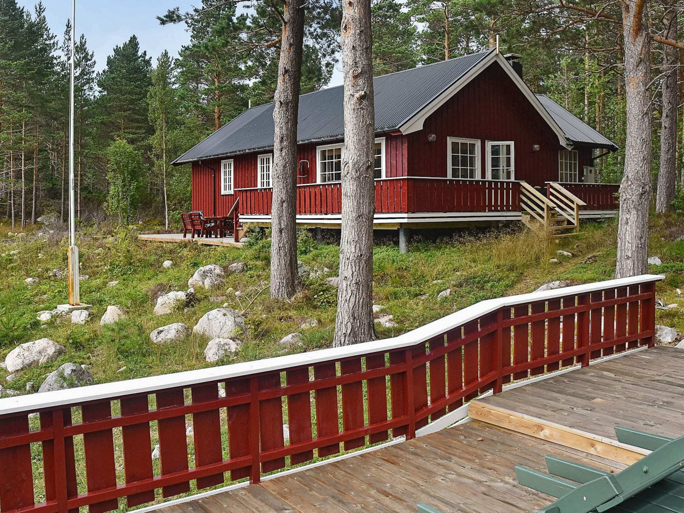 A red cabin with a deck, surrounded by trees and rocks.