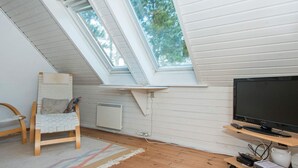 Ett rum med ett sluttande tak, en tv på ett träställ, en stol och ett litet bord med en fjärrkontroll.