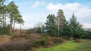 Ett grönområde med en träbänk, ett picknickbord och ett hus i bakgrunden.
