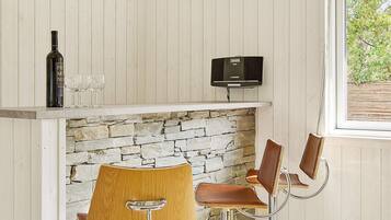A bar area with a stone fireplace, two bar stools, a wine bottle, and glasses.