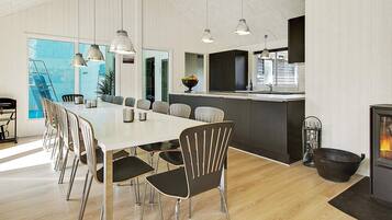 A modern kitchen with a central island, a dining area with a long table and chairs, and a fireplace.