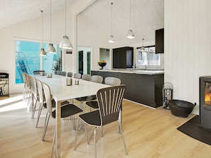 A modern kitchen with a central island, a dining area with a long table and chairs, and a fireplace. - 5 Star Holiday Home in Liseleje (Liseleje)