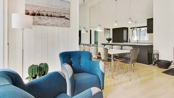 A spacious living area with a blue armchair, a dining table with chairs, and a kitchen area with pendant lights.
