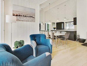 A spacious living area with a blue armchair, a dining table with chairs, and a kitchen area with pendant lights. - 5 Star Holiday Home in Liseleje (Liseleje)