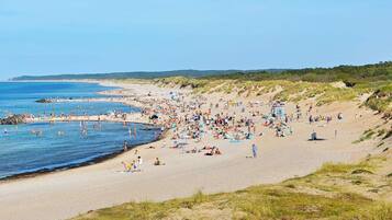 A beach with people sunbathing and swimming, sandy terrain, and a clear sky.