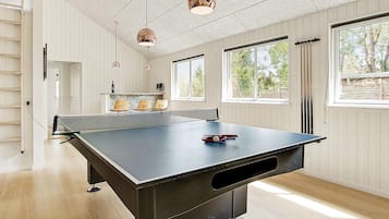 A ping pong table in a room with large windows, wooden walls, and pendant lights.