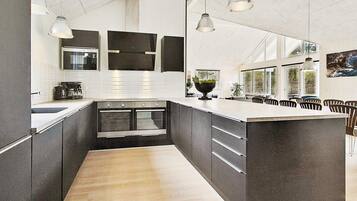 A modern kitchen with a large island, built-in ovens, pendant lighting, and a view of the outdoors.