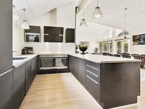 A modern kitchen with a large island, built-in ovens, pendant lighting, and a view of the outdoors. - 5 Star Holiday Home in Liseleje (Liseleje)