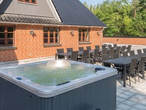 Un jacuzzi dans un jardin, avec une maison en briques, un coin salon extérieur et un toit recouvert de tuiles.