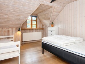 Une chambre avec un plafond en pente, une fenêtre, un radiateur, un lit, une table de chevet et une commode.