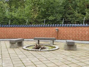Un espace extérieur aménagé avec un sol pavé, comprenant un foyer circulaire entouré de bancs.