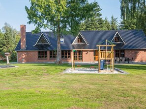 A brick building with a sloped roof, a swing set, and a fenced play area.