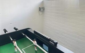 A room with a green floor, white walls, and a black ceiling. There are two white beds with black headboards and a white wardrobe.