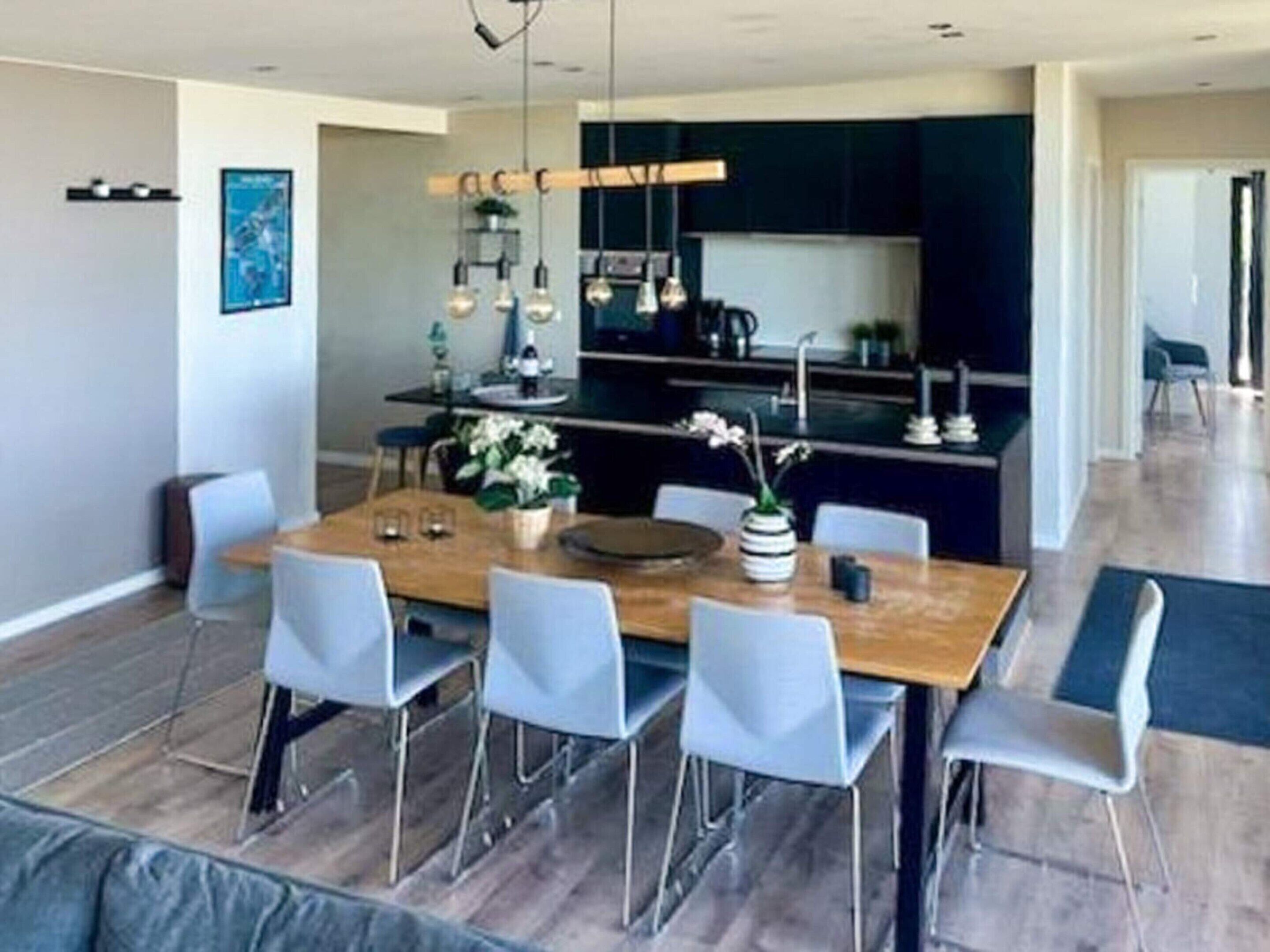 A modern dining area with a wooden table, six chairs, and hanging pendant lights.