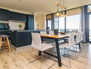 Una cocina moderna con armarios oscuros, una mesa de comedor de madera y vistas al mar a través de grandes ventanales.