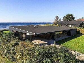 Una casa moderna con techo plano, un patio amplio abierto y vista al mar.
