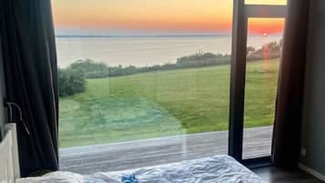 A bedroom with a view of the sea and a grassy area.