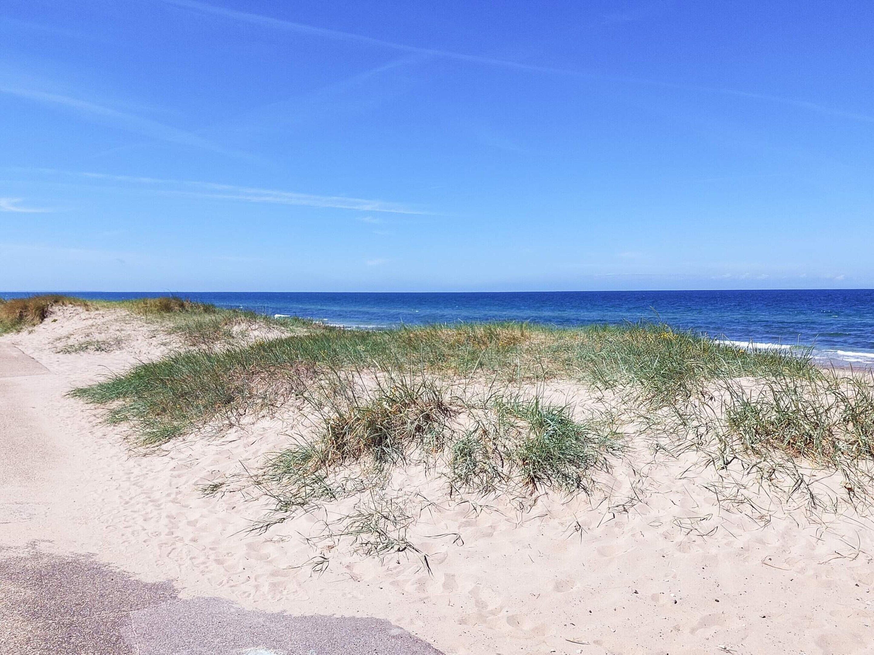 A sandy beach with dunes and a clear blue sky.