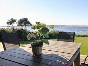A wooden table with a woven basket containing a plant, two chairs, and a view of the sea. - 8 Person Holiday Home in Olsted-by Traum (Olsted)